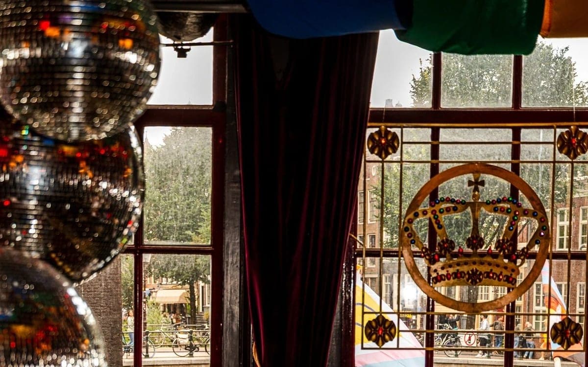Interieur van Café The Queen's Head in Amsterdam, met discoballen en uitzicht op de gracht.